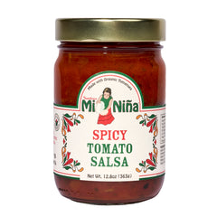 A 12.8 oz glass jar of Mi Niña Tortilla Spicy Tomato Salsa, featuring a gold lid and white label with a woman holding tomatoes and red-green patterns. Made with organic tomatoes. Sold in a convenient 6 pack.
